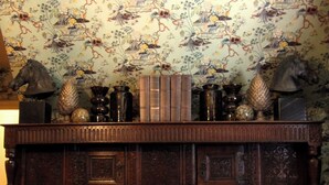 Un mueble de madera con intrincados grabados y un fondo de papel tapiz floral.