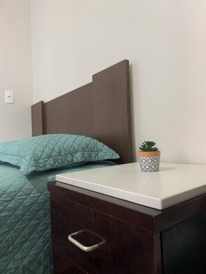 A bed with a quilted green blanket and pillows, a bedside table with a potted plant, and a drawer with a metal handle. - Suite with air conditioning and mini-bar next to Beto Carrero World (Penha)