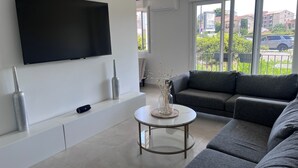 A modern living room with a flat-screen TV, grey sofa, and a glass coffee table. - 🏡 Bright apartment in Fréjus - beach, town center, night market (Fréjus)