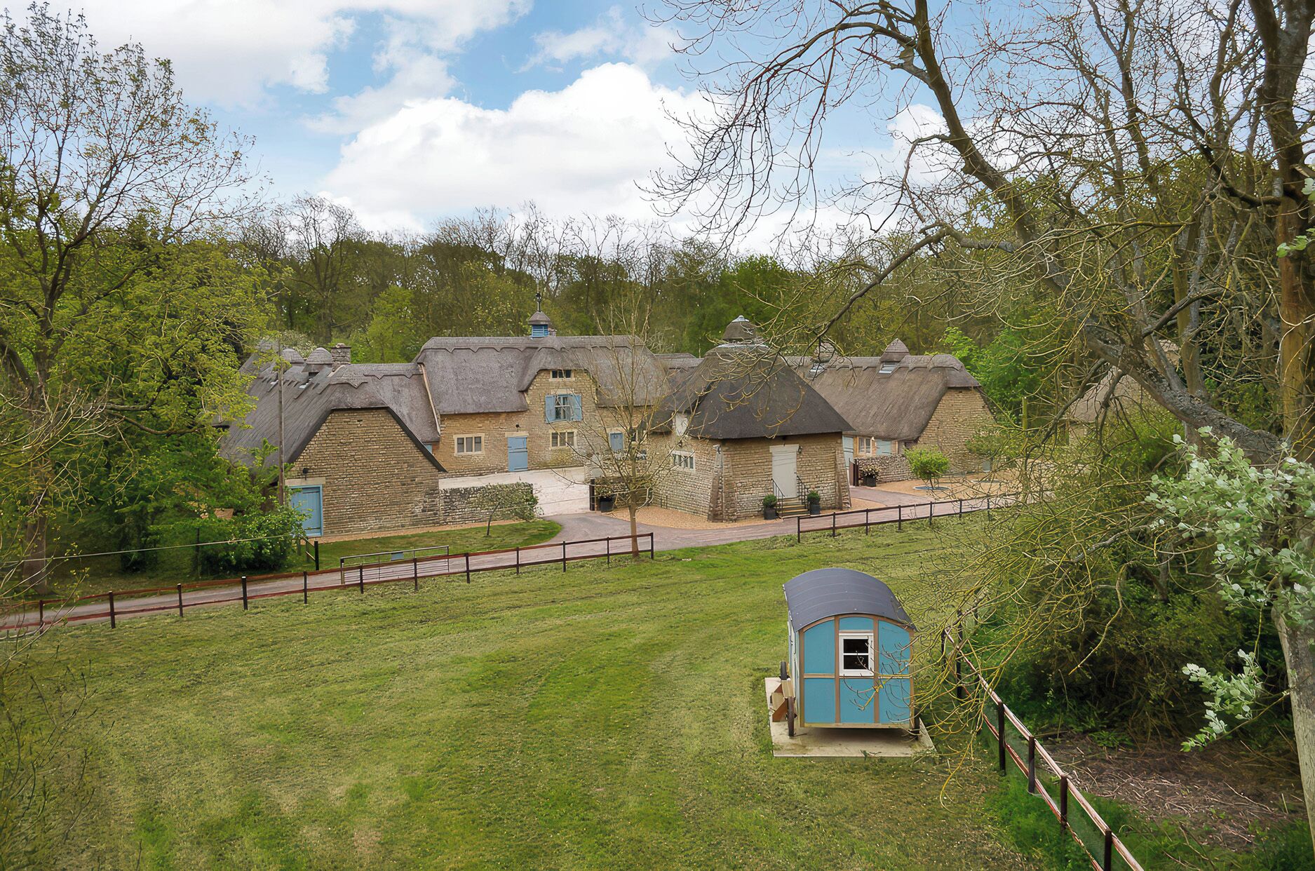 A traditional thatched-roof building with a stone exterior, surrounded by a grassy area and trees.