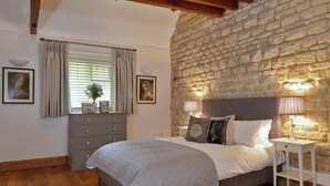 Un dormitorio con pared de piedra, cama con ropa de cama blanca, cómoda y dos lámparas de noche.