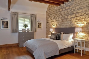 A bedroom with a stone wall, a bed with white bedding, a dresser, and two bedside lamps. - The Lady Rothschild Dairy (Peterborough)