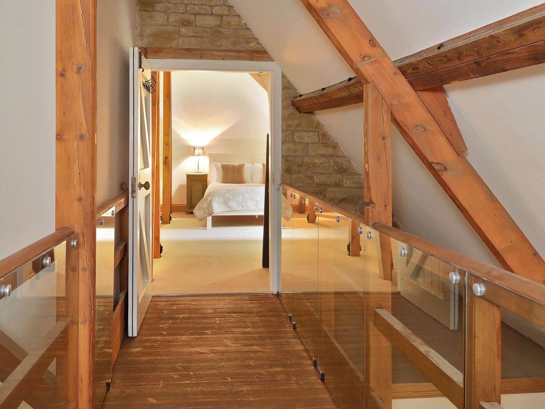 A wooden staircase leading to a bedroom with a stone wall, a bed, and a bedside lamp.