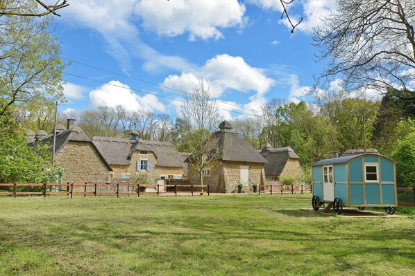 A traditional stone building with a thatched roof, a small blue structure, and a fenced area with benches. - The Lady Rothschild Dairy (Peterborough)