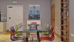 Un comedor con mesa de vidrio, sillas de colores, una escalera de madera y un cartel colgado en la pared.