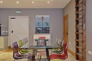 A dining area with a glass table, colorful chairs, a wooden ladder, and a wall-mounted poster. - The Lady Rothschild Dairy (Peterborough)