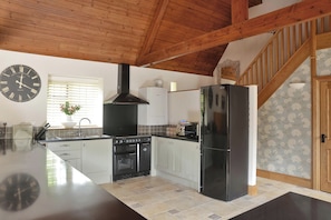 A kitchen with a black stove, oven, and refrigerator, wooden ceiling beams, and a clock on the wall. - The Lady Rothschild Dairy (Peterborough)