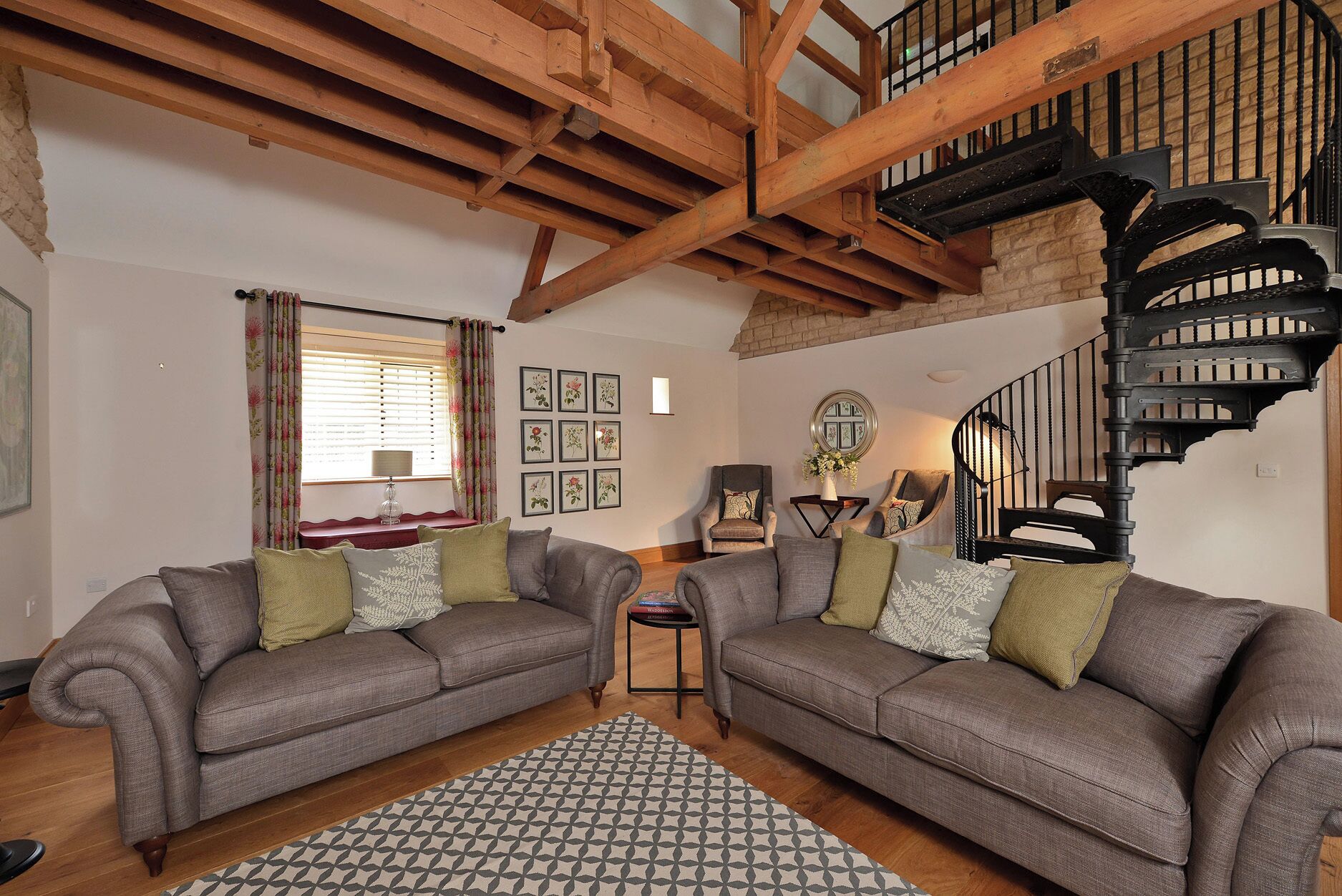 A living room with two sofas, a patterned rug, a staircase, and framed pictures on the wall.