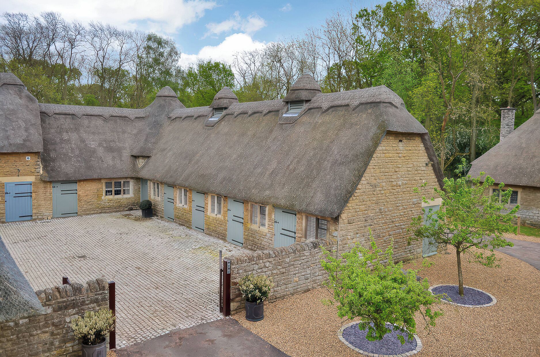 A traditional thatched-roof building with multiple windows and doors, surrounded by a cobblestone courtyard and trees.