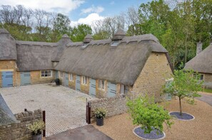 A traditional thatched-roof building with multiple windows and doors, surrounded by a cobblestone courtyard and trees. - The Lady Rothschild Dairy (Peterborough)