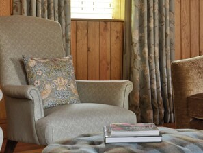 A room with a patterned armchair, a cushion with a floral design, and a book on a table. - The Lady Rothschild Dairy (Peterborough)