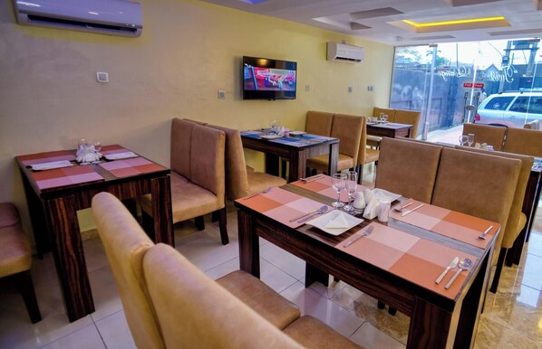 A restaurant with tables set for dining, a television mounted on the wall, and a view of the street outside. - Twist Hotels (Lagos)