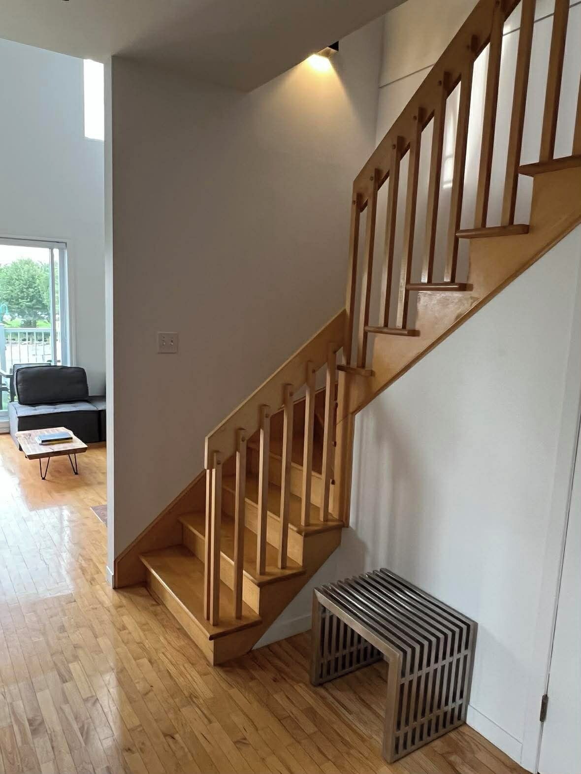 A modern staircase with wooden railings and a metal handrail, leading to a room with a wooden floor and a black sofa.