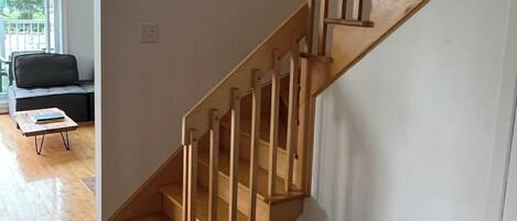 A modern staircase with wooden railings and a metal handrail, leading to a room with a wooden floor and a black sofa.