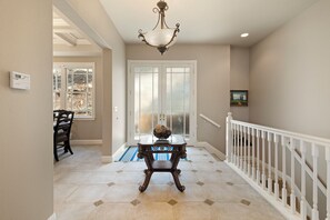 A hallway with a white railing, a table with a decorative bowl, and a door leading outside.