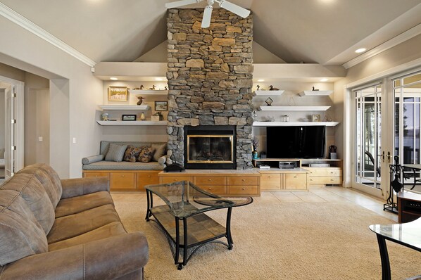 A living room with a stone fireplace, a sofa, a glass coffee table, and a television.