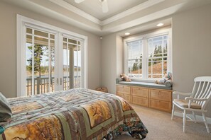 A bedroom with a large bed, a window seat, a chair, and a view of the outdoors.