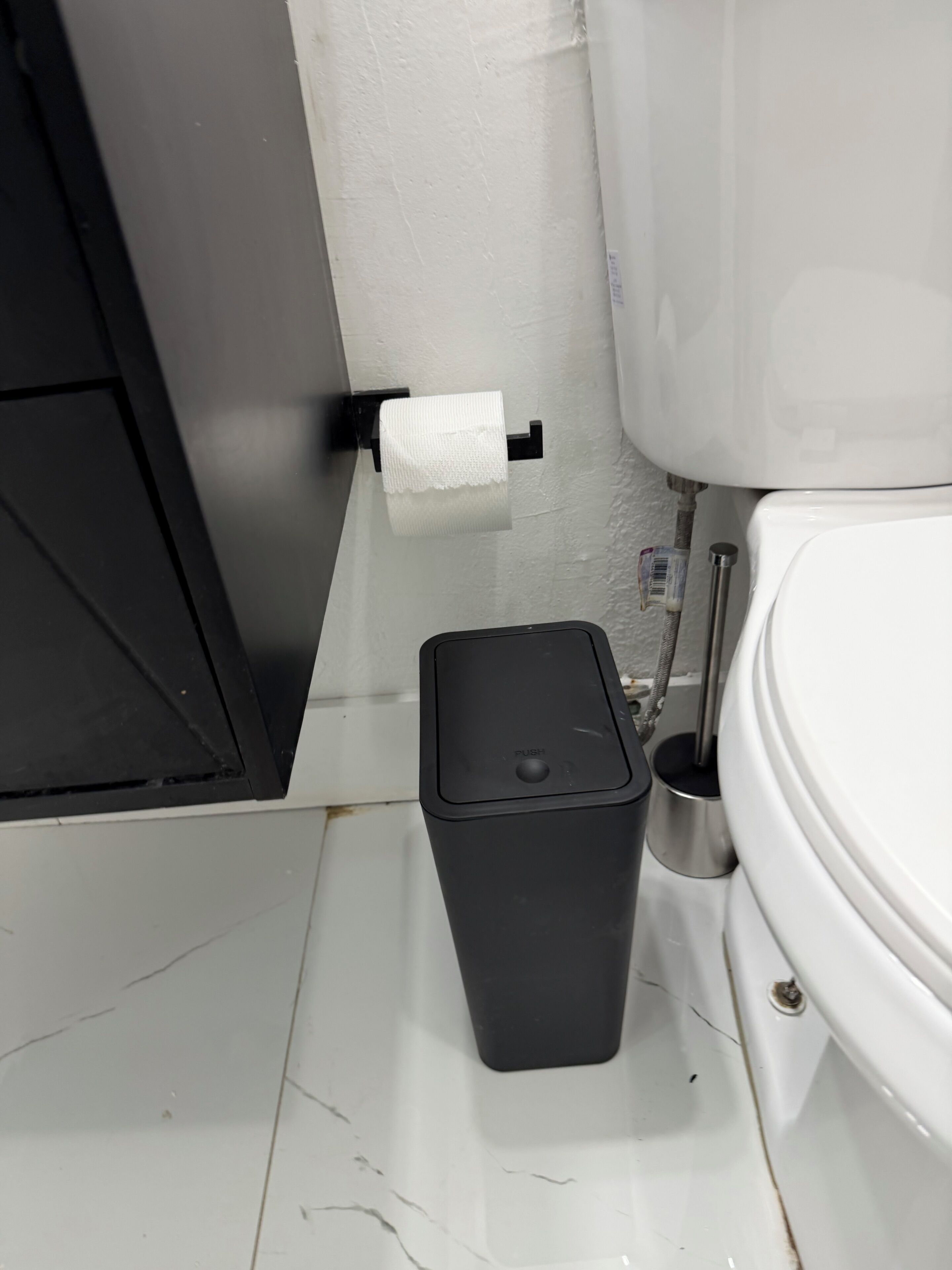 Un baño con inodoro, un bote de basura y un dispensador de toallas de papel en la pared.