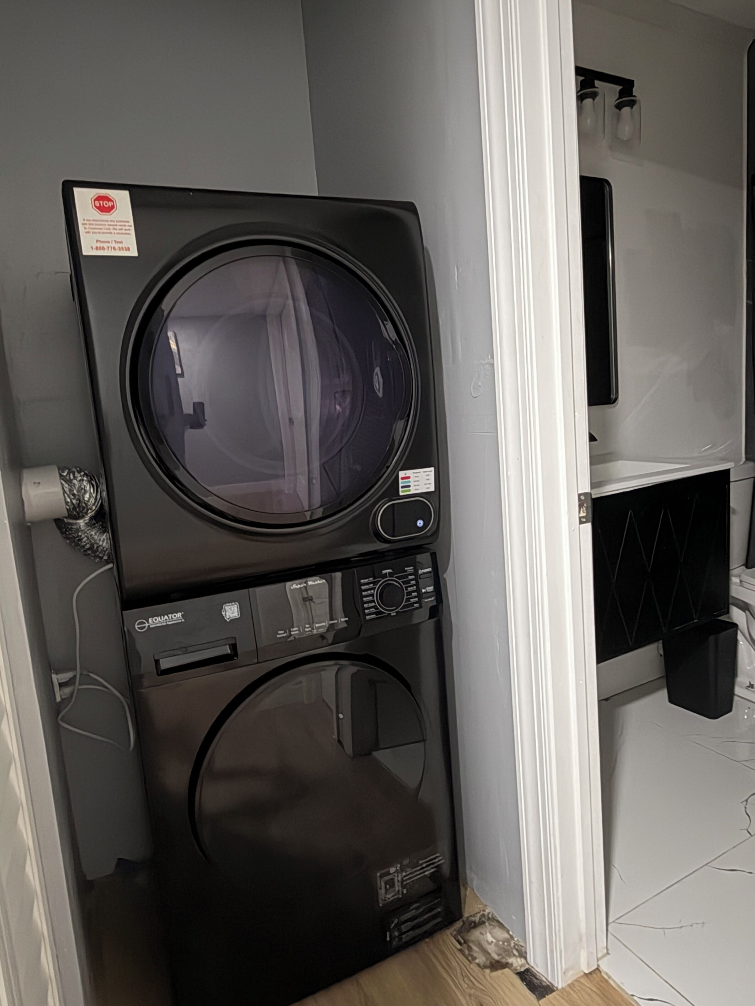 A compact washer and dryer unit in a corner of a room with a white wall and a small window.