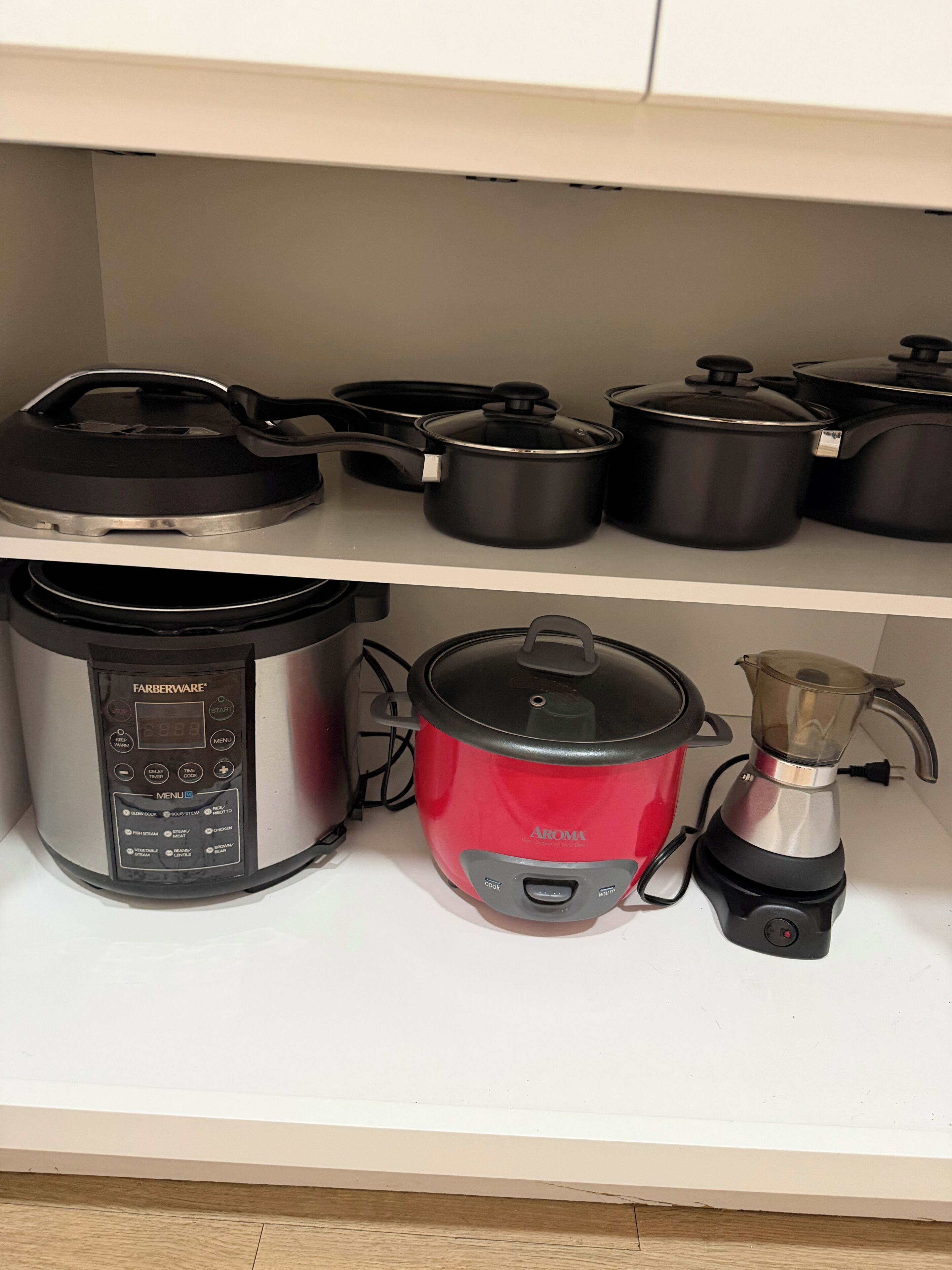 Une cuisine équipée d’une mijoteuse Farberware, d’un cuiseur à riz rouge de la marque Aroma et d’une machine à café posée sur le plan de travail.