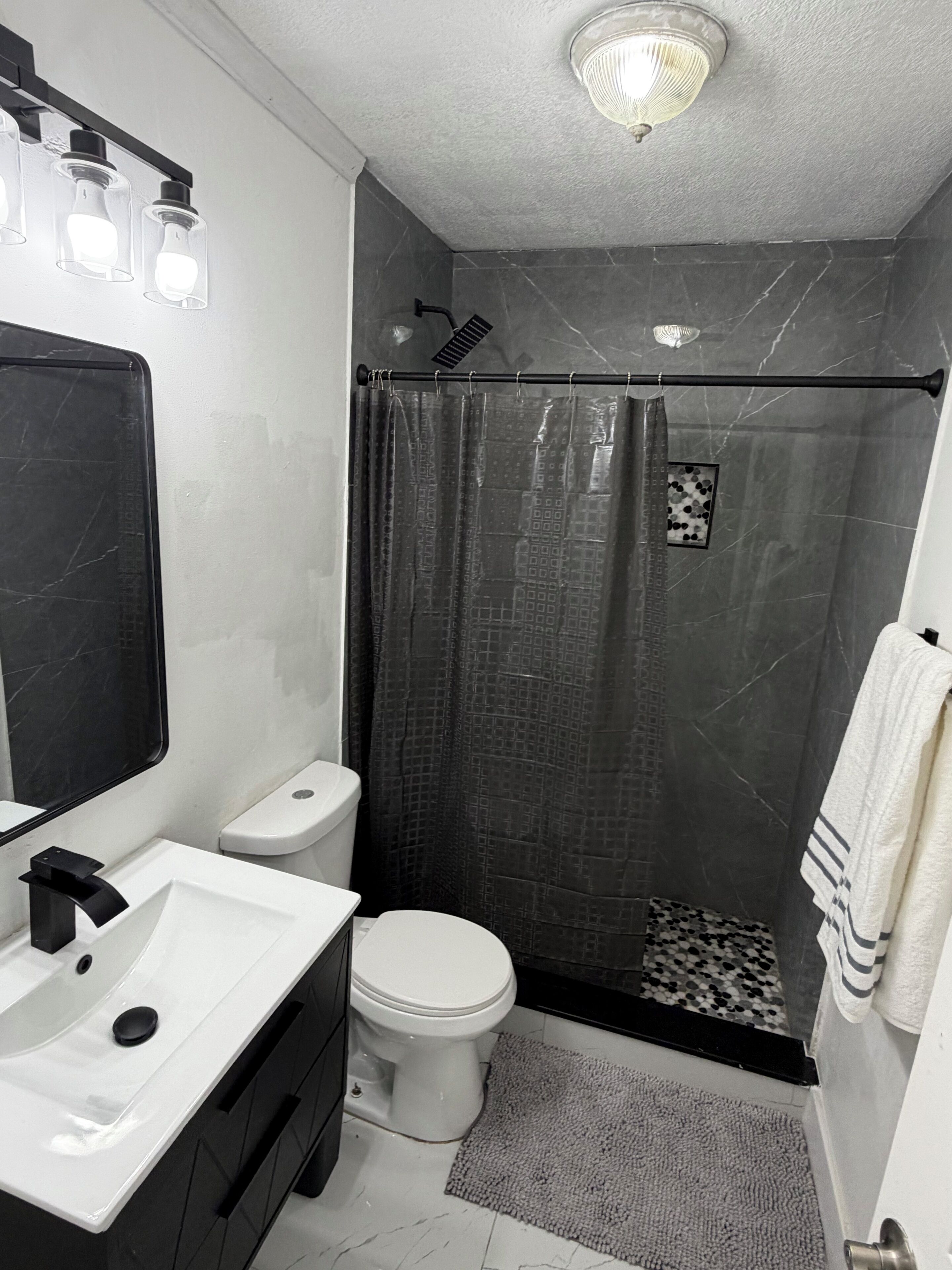 Een badkamer met een wit wastafelmeubel, een zwart kastje, een wit toilet en een douche met een donker gordijn.