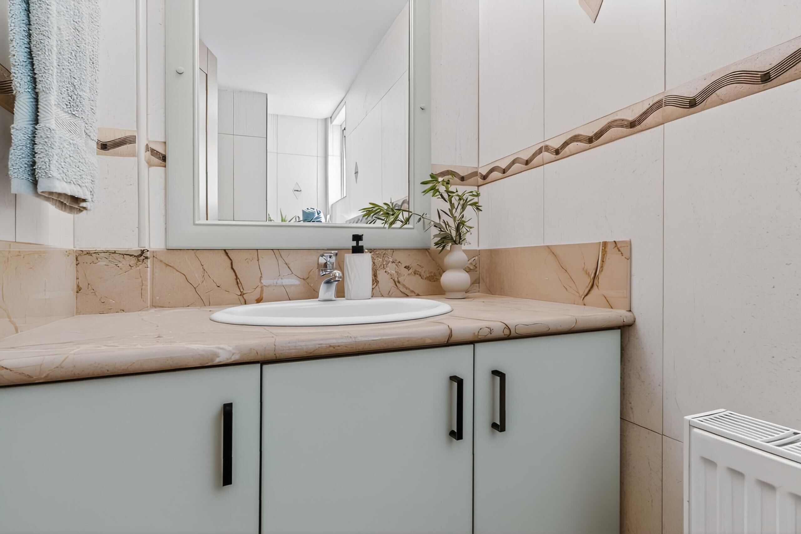 A bathroom with a white sink, a mirror, a towel rack, and a radiator.