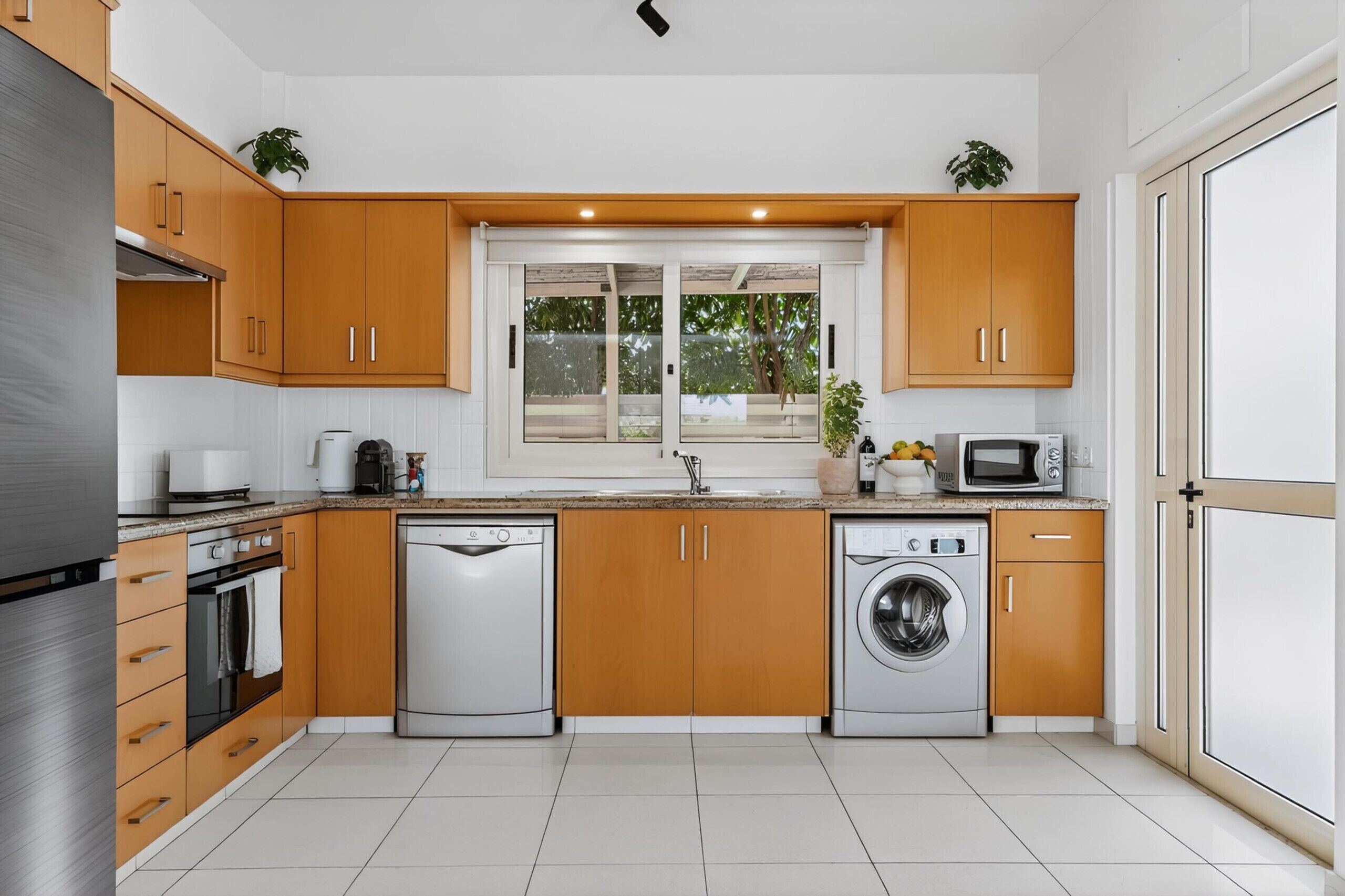 Une cuisine moderne avec des meubles en bois, des appareils électroménagers en acier inoxydable et une fenêtre donnant sur les arbres.