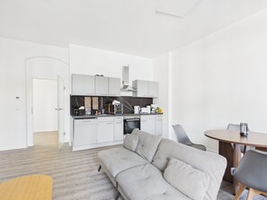 A modern kitchen with white cabinets, a built-in oven, and a dining area with a round table and chairs. - Family apartment with balcony, up to 5 guests - GÖ06 (Görlitz)