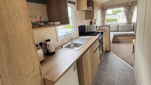 A compact kitchenette with a sink, stove, and microwave. - Caravan Sleeps 5 - Decking, Parking, Pet Friendly (Blackpool)