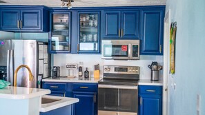 A kitchen with blue cabinets, a stainless steel refrigerator, a coffee maker, and a microwave.