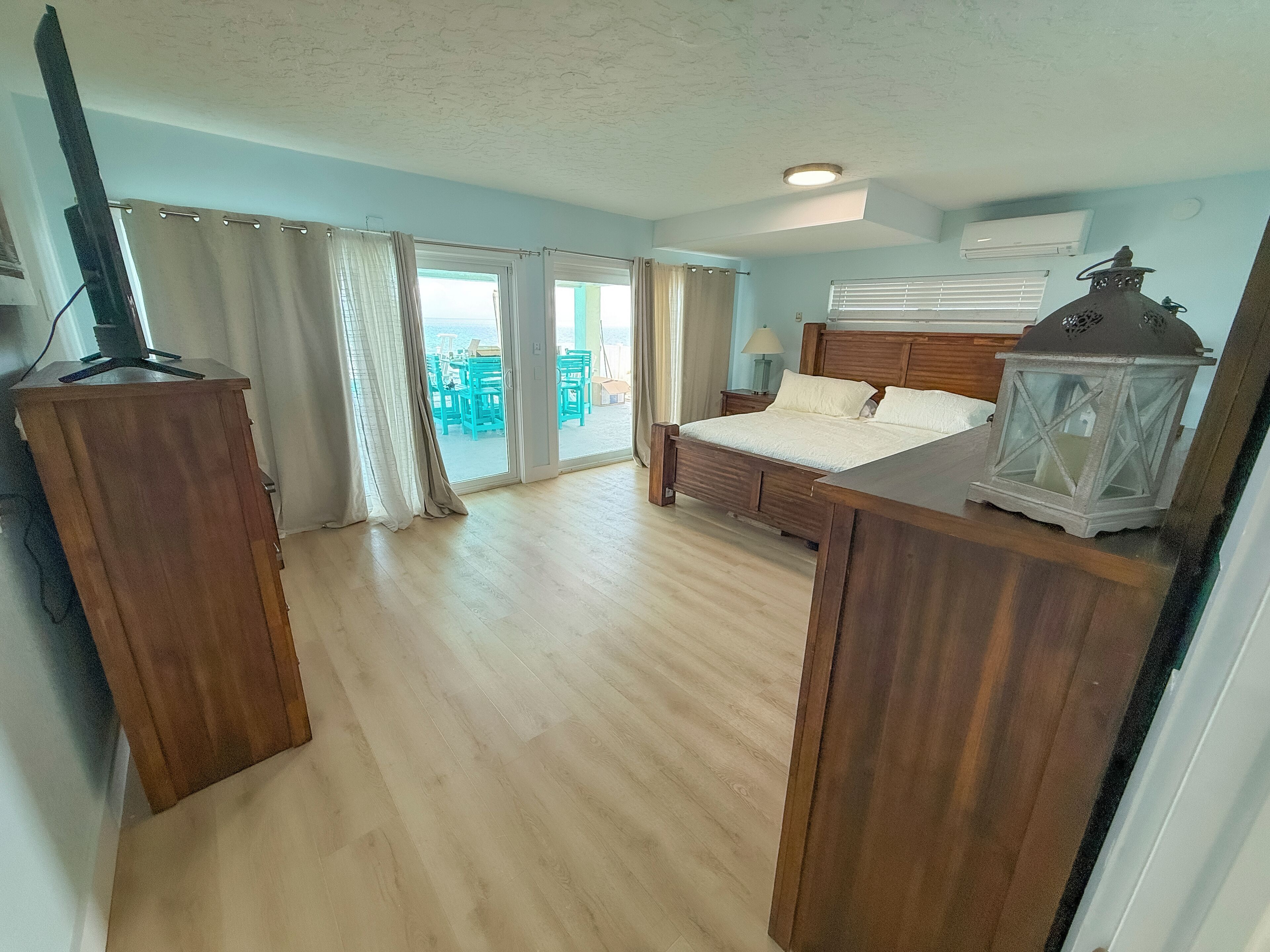 A bedroom with a bed, curtains, a wooden desk, a television, and a view of the outside.