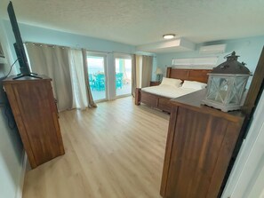 Un dormitorio con cama, cortinas, un escritorio de madera, televisor y vistas al exterior.
