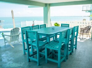 A covered outdoor area with a table and chairs, a view of the ocean, and a white fence. - Marathon Oceanfront 4BR, 3.5BA Private Pool 60’ Boat Dock (Marathon)