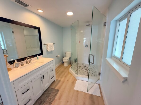Une salle de bain moderne avec une douche à parois de verre, un grand miroir et un meuble-lavabo blanc.