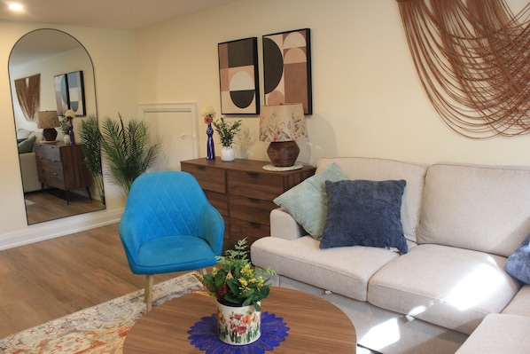 Ein Wohnzimmer mit blauem Sessel, beiger Couch, Holz-Couchtisch und einer dekorativen Vase.