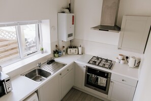 Eine moderne Küche mit Gasherd, Backofen, Spüle und einem Fenster mit Blick auf eine Holzterrasse.