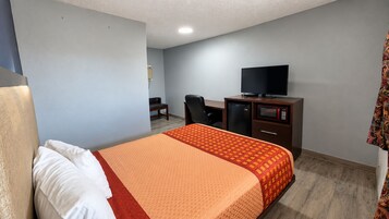 Una habitación de hotel con una cama, un escritorio con computadora, televisor y microondas.