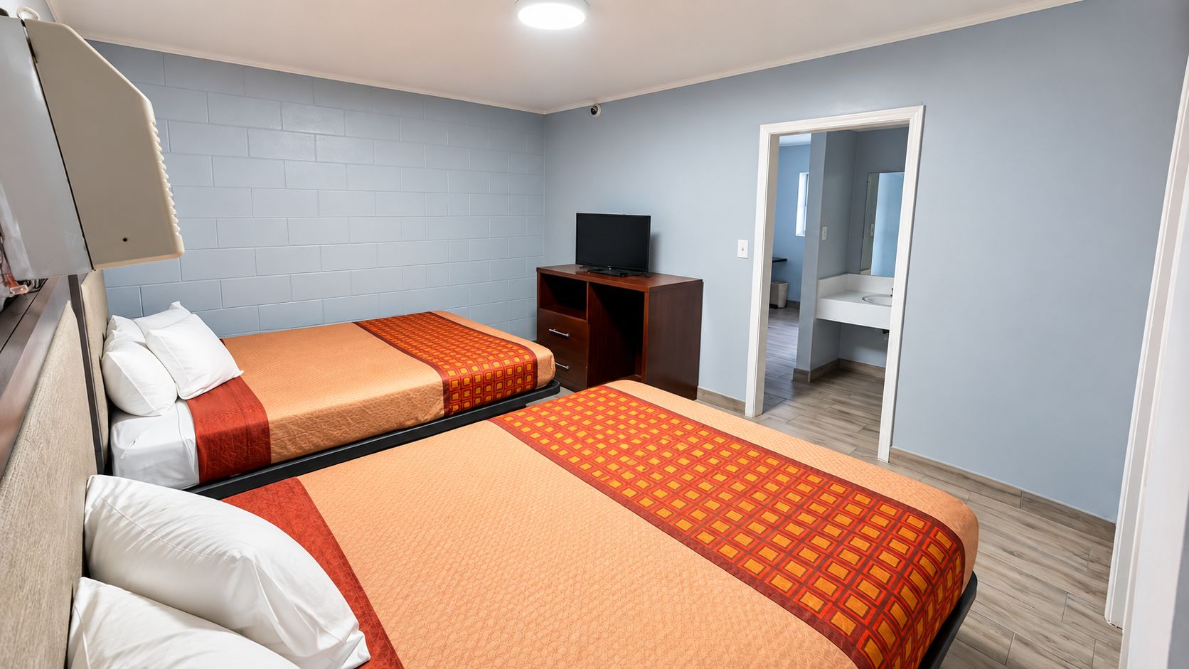 A hotel room with two beds, a TV, a wardrobe, and a bathroom visible through an open door.