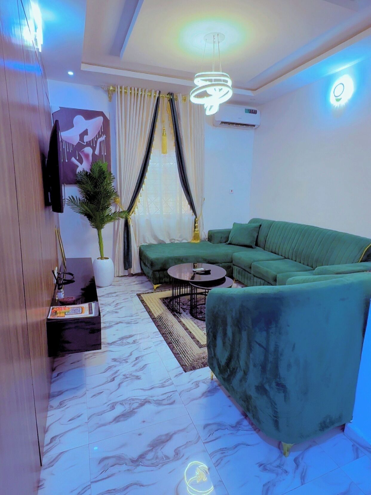Ein modernes Wohnzimmer mit einem grünen Sofa, einem kleinen Couchtisch, einem an der Wand montierten Fernseher und einem Blumentopf.