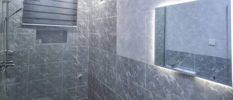 A modern bathroom with a shower, toilet, and sink, featuring marble tiles and a glass shower enclosure.