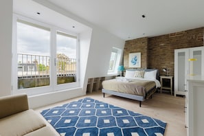 Une chambre avec une grande fenêtre, un lit, un tapis à motifs bleus et un mur en briques.