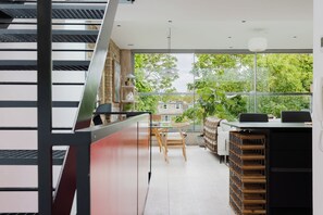 Un intérieur moderne avec un escalier, un coin repas comprenant une table et des chaises, et une vue sur la verdure à l’extérieur.