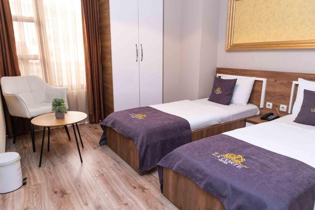 A hotel room with two beds, a chair, a small table, and a wardrobe.
