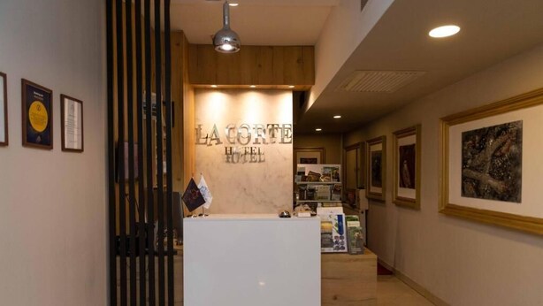 Una mesa de recepción con un cartel que dice 'La Corte Hotel' y certificados enmarcados en la pared.