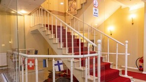 Una escalera con balaustres blancos, peldaños cubiertos de alfombra roja y banderas.
