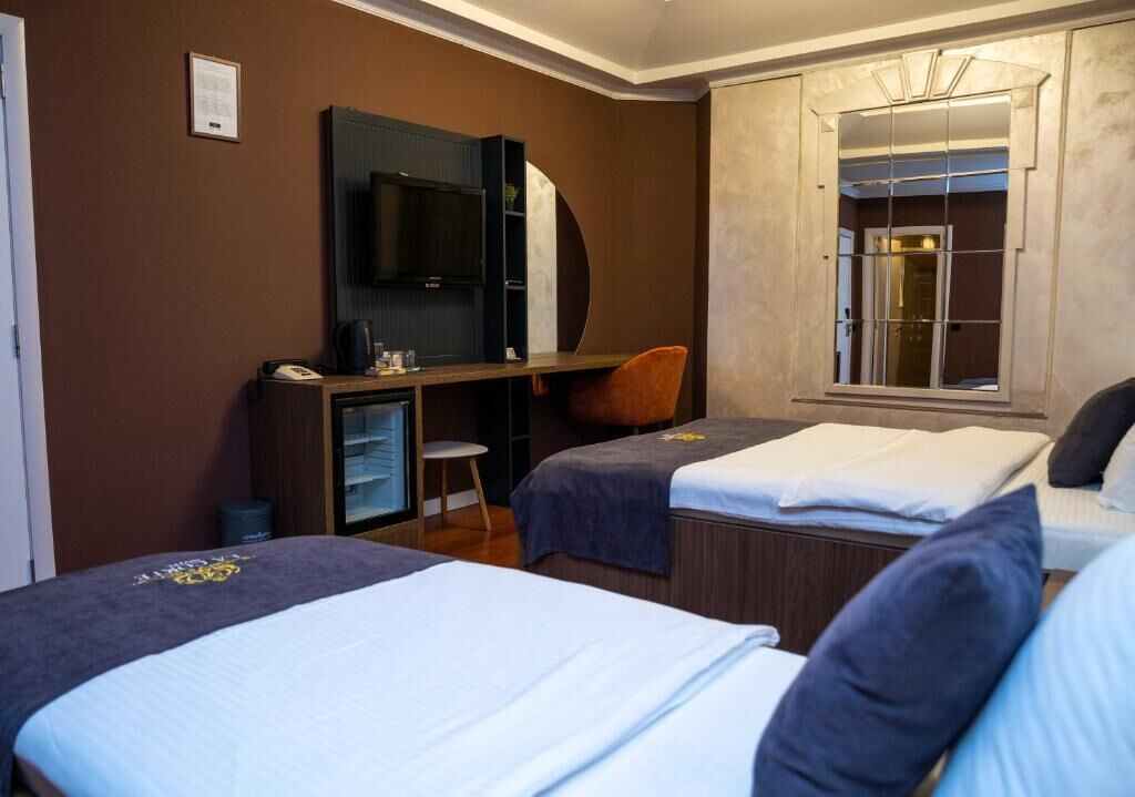 Une chambre d’hôtel avec deux lits, un bureau avec une chaise, une télévision et un grand miroir.