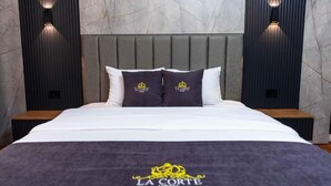 Una habitación de hotel con cama, almohadas, cabecera, mesitas de noche y apliques de pared.