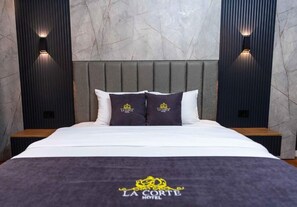 Una habitación de hotel con cama, almohadas, cabecera, mesitas de noche y apliques de pared.
