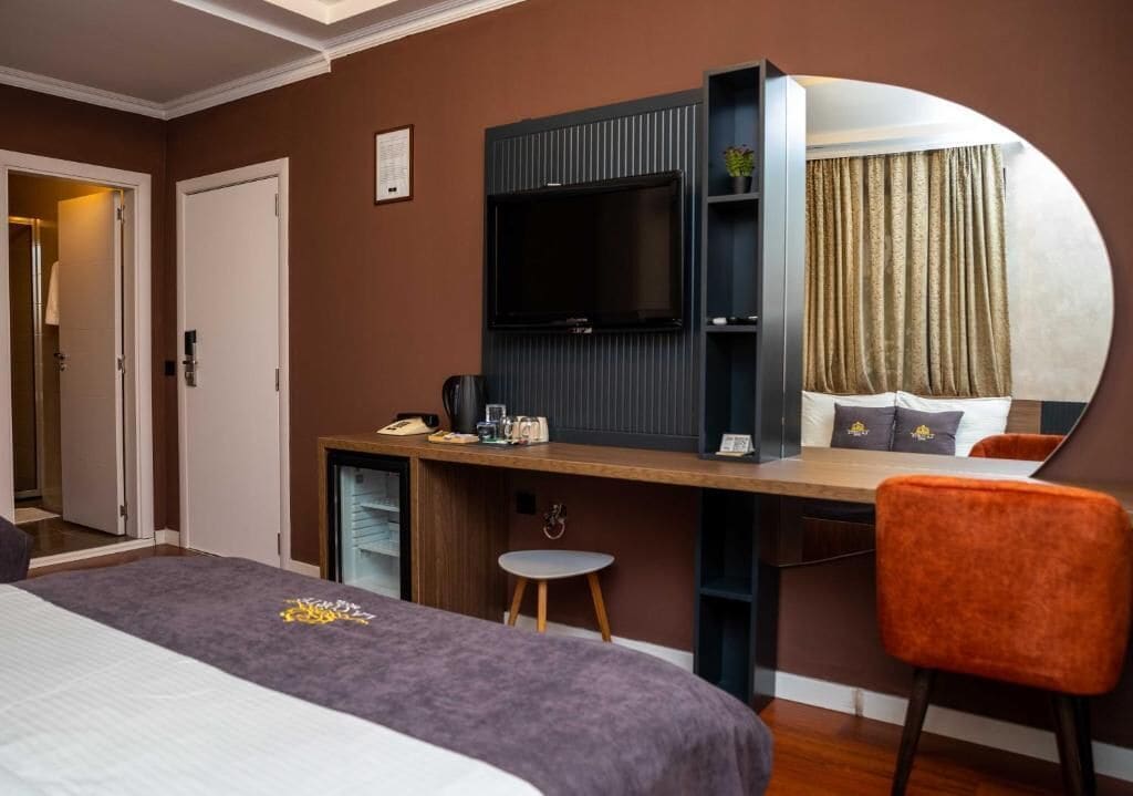 A hotel room with a bed, a desk with a TV, a chair, and a mirror.
