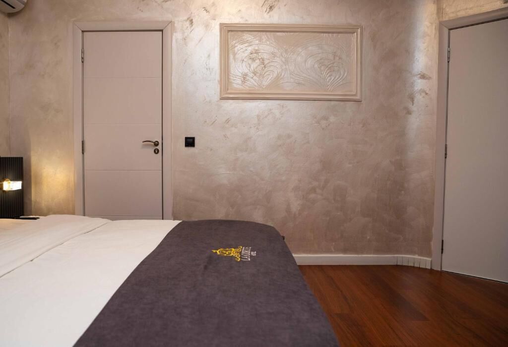 A bedroom with a bed, a door, a wall-mounted artwork, and a carpeted floor.